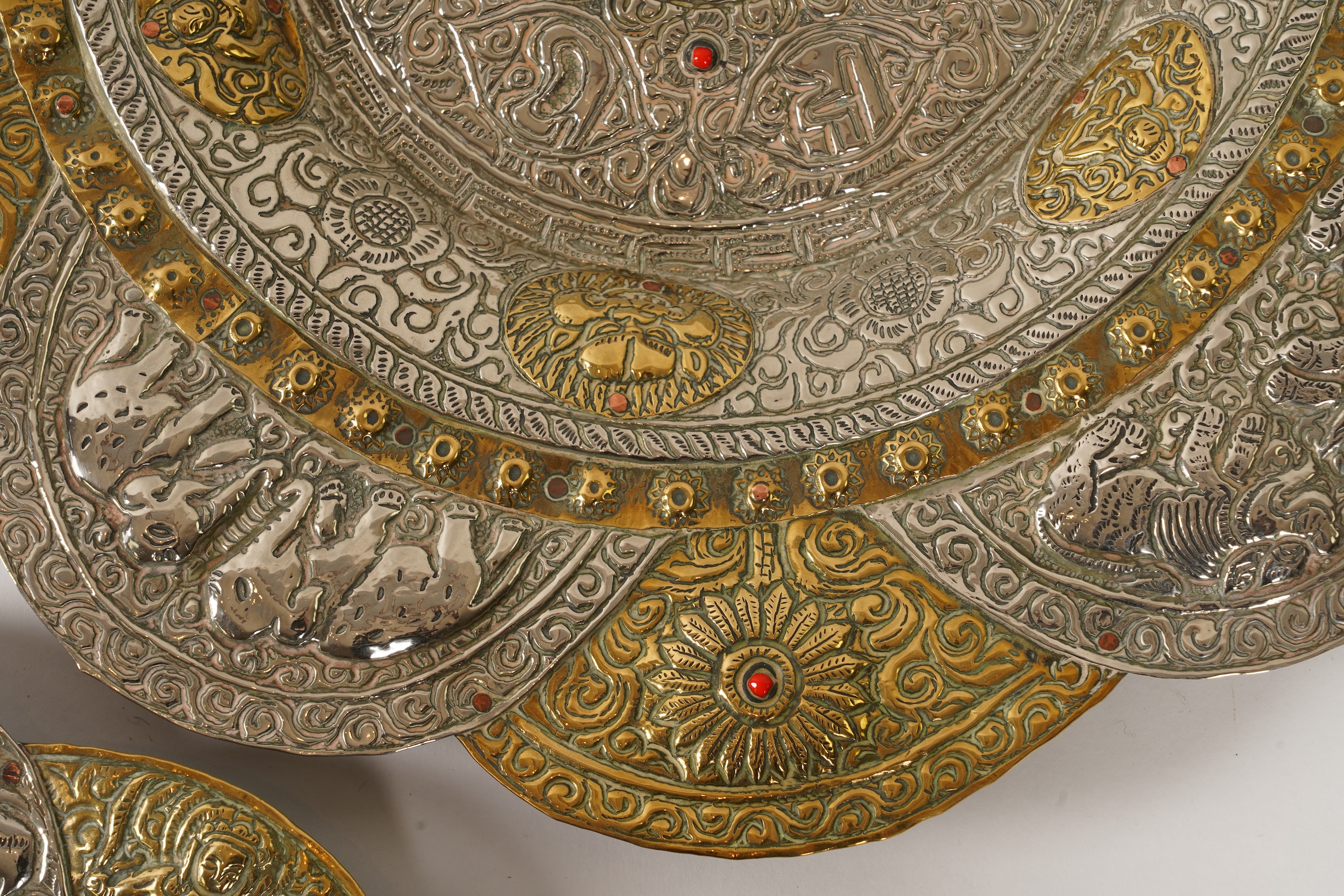 A graduated set of three Nepalese repoussé white metal and brass chargers, first half 20th century